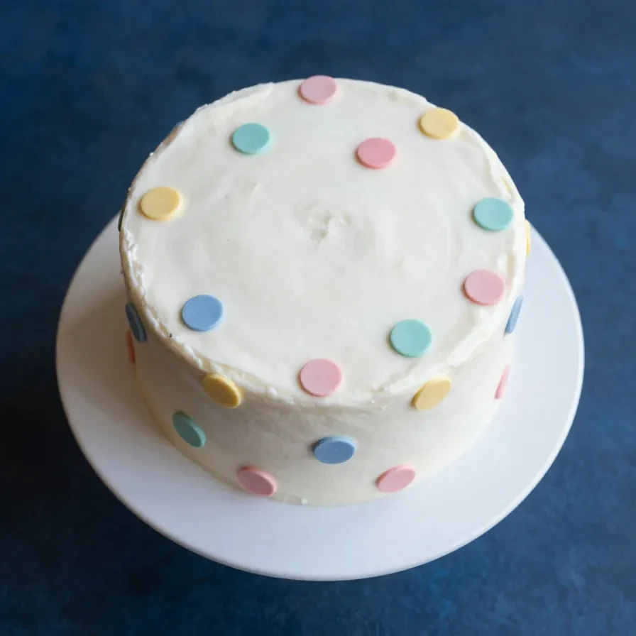 A freshly baked vanilla polka dot cake with colorful sprinkles on a wooden table.